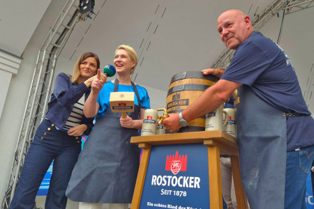 Mit drei kräftigen Hammerschlägen eröffnete Ministerpräsidentin Manuela Schwesig (M.) beim Fassbieranstich der Hanseatischen Brauerei Rostock die 87. Warnemünder Woche. Unterstützt wurde sie von Braumeister Holger Köpcke (l.), der nach 47 Jahren in den Ruhestand geht. Frauke Raunert (r.), NDR MV, moderierte die feierliche Zeremonie.