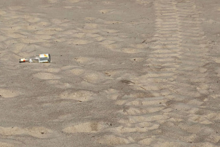 Das Foto von Beiratsmitglied Mathias Stagat zeigt eine Glasflasche im Strandsand. Die direkt daneben befindliche Traktorspur lässt die Vermutung zu, dass hier gerade die Reinigung erfolgte.