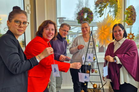 Vor dem festlich geschmückten Wunschbaum im Windfang versammeln sich Rezeptionsmitarbeiterin Lisa Ryll, Hotelchefin Katharina Soyk, Teamleiter Kai Joest sowie die beiden liebevollen ‚Pflegemamas‘ Ute B. und Tanja S. – ein Team, das gemeinsam Weihnachtswünsche wahr werden lässt.