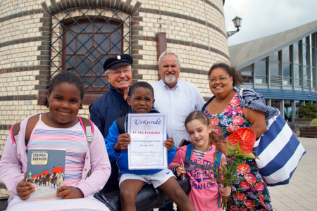 Der sechsjährige Tai (3.v.l.) aus England wurde heute als der 60.000. Leuchtturmbesucher des Jahres bestimmt. Gemeinsam mit Schwester Tia (8), Mama Gina und Freundin Emilia (6) besucht er das Warnemünder Wahrzeichen zum ersten Mal. Schatzmeister Walter Vogt und Leuchtturmchef Klaus Möller heißen die Gäste herzlich willkommen.