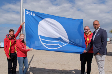 Die beiden Rettungsschwimmer Max Cornelius, Sarah Wenzel sowie DRK-Wachleiter Lukas Knaup und Matthias Fromm (v.l.) hissen am Strandaufgang 10 in Warnemünde die Blaue Flagge. 