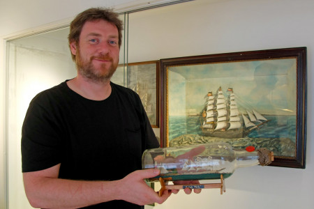 Buddelschiffe waren eine typische kunsthandwerkliche Bastelarbeit der Seeleute des 19. und 20. Jahrhunderts. Museumsleiter Christoph Wegner hält eine Arbeit von Fiete Harms mit dem Segelschulschiff „Gorch Fock“ in den Händen.
