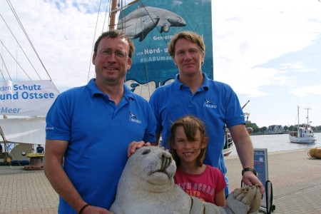 Nabu-Bundesgeschäftsführer Leif Miller (l.) mit Töchterchen Marla und Meeresschutzexperte Dr. Kim Detloff vor dem Traditionssegler "Ryvar", mit dem sie zehn Tage lang auf Ost- und Nordsee unterwegs sind.