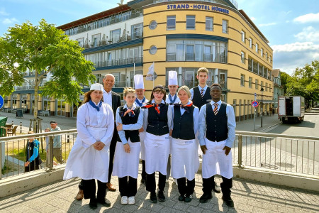 Freuen sich auf neue Herausforderungen im Hotel Hübner Warnemünde: Reihe hinten v.l. Hoteldirektor Dietmar Karl, Artem Levschenko, Sebastian Wiegandt (beide Azubi Koch), Jannes Heymann (Azubi Hotelfachmann), Reihe vorn v.l. Ekaterine Moistsrapeshvili (Azubi Koch), Louise Levin (Azubi Restaurantfachfrau), Maria Gabel (Azubi Hotelfachfrau), Lucy Celine Fischer und Nazifou Oussou (beides Azubi Restaurantfachfrau)//Foto: Hotel Hübner Freuen sich auf neue Herausforderungen im Hotel Hübner Warnemünde: Reihe hinten v.l. Hoteldirektor Dietmar Karl, Artem Levschenko, Sebastian Wiegandt (beide Azubi Koch), Jannes Heymann (Azubi Hotelfachmann), Reihe vorn v.l. Ekaterine Moistsrapeshvili (Azubi Koch), Louise Levin (Azubi Restaurantfachfrau), Maria Gabel (Azubi Hotelfachfrau), Lucy Celine Fischer und Nazifou Oussou (beides Azubi Restaurantfachfrau)//Foto: Hotel Hübner