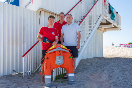 Sven Hennig und Ronald Hennig von der DRK Wasserwacht Rostock pr&auml;sentieren gemeinsam mit J&uuml;rgen Breuer (v. l.), Gesch&auml;ftsf&uuml;hrer der Rostocker Dach-Bau GmbH, am Strand von Warnem&uuml;nde einen der neuen Wasserrettungsroboter vom Typ &bdquo;Dolphin 3&ldquo;. Die moderne Technik soll Rettungseins&auml;tze an der Ostseek&uuml;ste k&uuml;nftig noch sicherer machen.//Foto: DRK, Junge