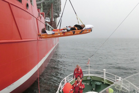 Mit einem Kran wird die spezielle Bergungstrage der DGzRS mit dem erkrankten Seemann auf den Seenotrettungskreuzer „Arkona“ heruntergelassen.