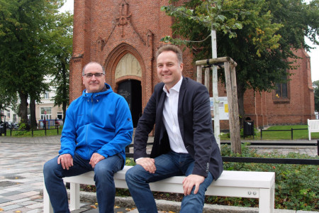 Prima Sitzkomfort: Pastor Harry Moritz und Senator Holger Matthäus probieren die neuen Bänke auf dem Kirchenplatz aus.