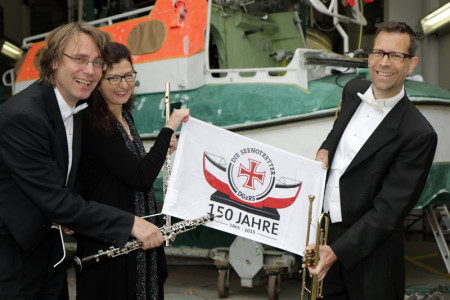 "Bootschafter" der Seenotretter war in diesem Jahr die Deutsche Kammerphilharmonie Bremen. Musiker des Orchesters präsentierten jetzt die vorläufigen Einsatzzahlen bis Ende Oktober. Ulrich König (Oboe), Ulrike Höfs (Querflöte) und Bernhard Ostertag (Trompete) vor der Werfthalle der Seenotretter in der Zentrale in Bremen, im Hintergrund das Tochterboot des Seenotrettungskreuzers "Vormann Jantzen", das derzeit hier überholt wird.