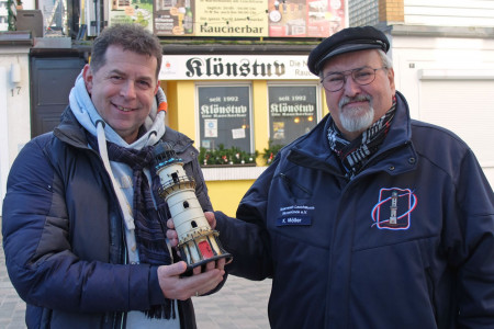 René Kroboth-Stolte (l.) überreicht eine prall gefüllte Leuchtturm-Sparbüchse an Klaus Möller. Das Geld summiert sich aus dem Glühweinverkauf beim Adventssingen und den Spenden für das Warnemünder Turmleuchten. 