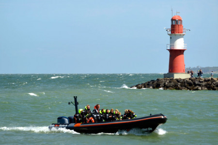 Ein mit Urlaubsgästen voll besetztes hochmotorisiertes Schlauchboot passiert die Warnemünder Molenköpfe. 
