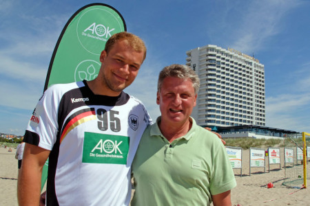 Handball-Nationalspieler Paul Drux (l.) hat Wort gehalten und die Sonne mit an den AOK Active Beach Warnemünde gebracht. Cheftrainer Andreas Zachhuber freut sich über den prominenten Besuch.