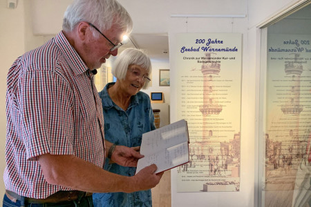 Der stellvertretende Vorsitzende des Museumsvereins, Werner Kreuscher, und Gabi Köbbert, Mitglied des Museumsvereins, blättern im Gästebuch zur Sonderausstellung „200 Jahre Seebad Warnemünde“, die noch bis zum 14. August zu sehen ist.