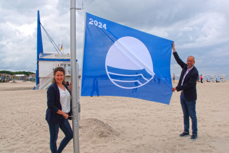 Denise Johannsson von der Tourismuszentrale und Tourismusdirektor Matthias Fromm hissen die Blaue Flagge 2024 am Warnemünder Strand.