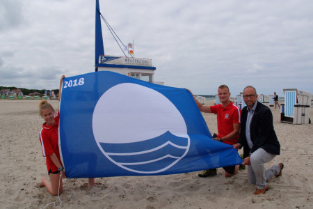 Sie hissen die „Blaue Flagge“ am Strand von Warnemünde: die Rettungsschwimmer der DRK-Wasserwacht Alexandra Sievert und Arian Baume und Tourismusdirektor Matthias Fromm (v.l.).