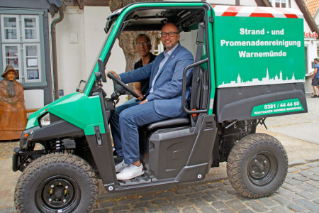 Tourismusdirektor Matthias Fromm (vorn) und Frank Bose, Geschäftsführer Rostocker Gehweg Reinigung, präsentieren das neue Elektro-Fahrzeug zur Unterstützung der Standreinigung in Warnemünde.