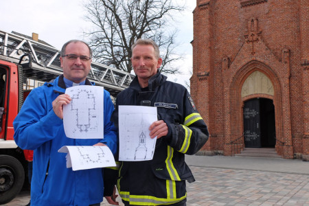 Pastor Harry Moritz (li.) unterstützt das Vorgehen der Feuerwehr und überreicht an den verantwortlichen Brandmeister Christian Lechner Grundriss und Querschnitt der Warnemünder Kirche.