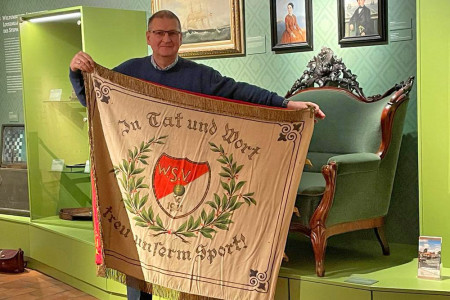 Uwe Heimhardt zeigt die prächtige Fahne des Warnemünder Sport Vereins 1911, die das Heimat-museum erwerben konnte und nun restauriert werden soll. Foto: Sabine Schubert