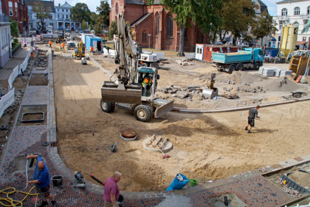 Die Arbeiten auf der Großbaustelle Kirchenplatz Warnemünde gehen sehr gut voran. Am Freitag trägt ein Asphaltfertiger die Schwarzdecke auf.