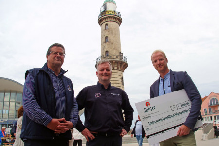 Bastian Pochstein von der Lübzer Brauerei (r.) kam mit einem symbolischen Scheck über 6.000 Euro nach Warnemünde. Damit wird der Leuchtturmverein, vertreten durch Mathias Stagat (m.) und Andreas Herpoldt, für sein gesellschaftliches Engagement geehrt.