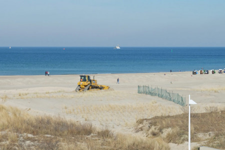 Eine Planierraupe verteilt die Sandmassen am Warnemünder Strand.