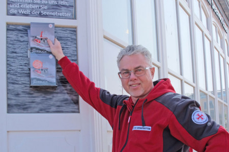 Der Leiter des Seenotretter Informationszentrums Warnemünde, Jörg Westphal, beim Befüllen des Infokastens an der Hausecke, Am Leuchtturm 1.