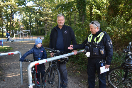 Mathias Stagat (Mitte) und sein sechsjähriger Sohn Ansgar lassen sich durch den Kontaktbeamten Karsten Meyer erklären, wie man sicher vom Spielplatz auf den Fahrradweg Parkstraße kommt.